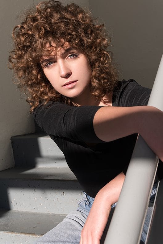 A young woman with curly hair leaning on stairs.