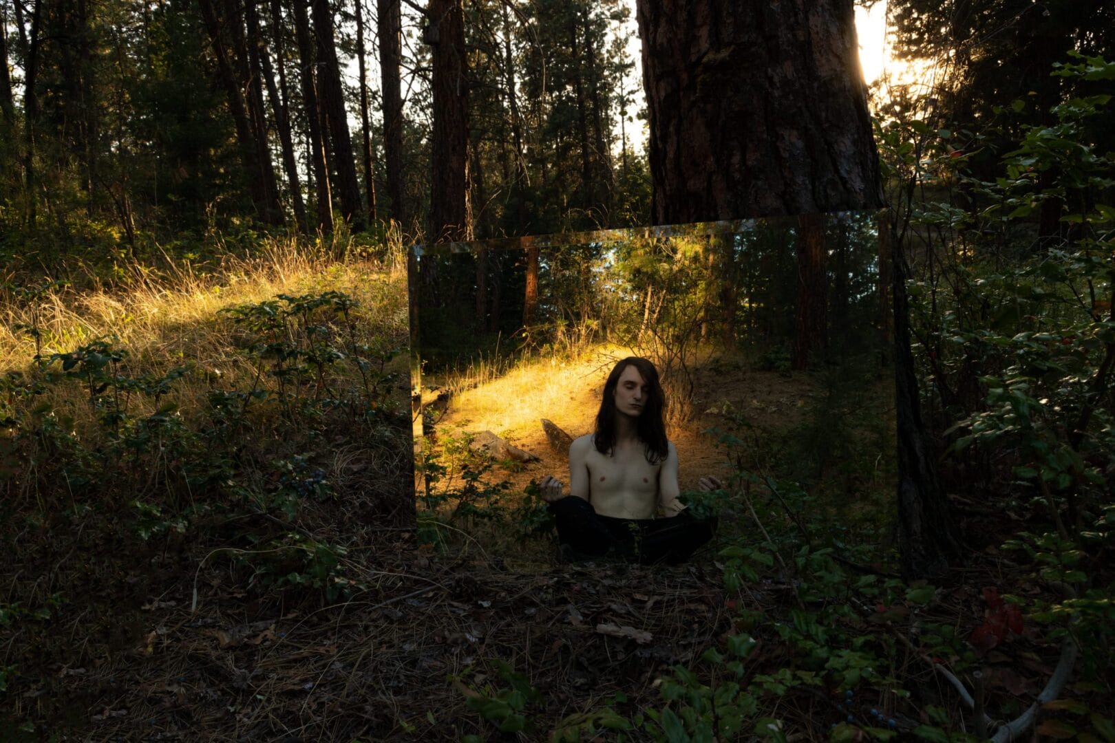 A woman sitting in the woods in front of a mirror.